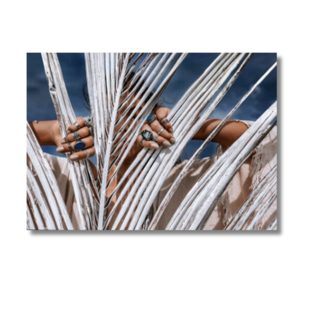 CLOSE UP OF BEAUTIFUL YOUNG TRIBAL STYLE WOMAN WITH LOTS OF ACCESSORIES BEHIND PAINTED WHITE PALM LEAF