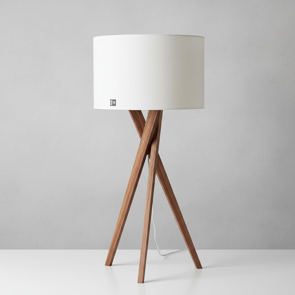 A table lamp with a white lampshade and brown wooden tripod base, standing next to a stack of books on a white surface.