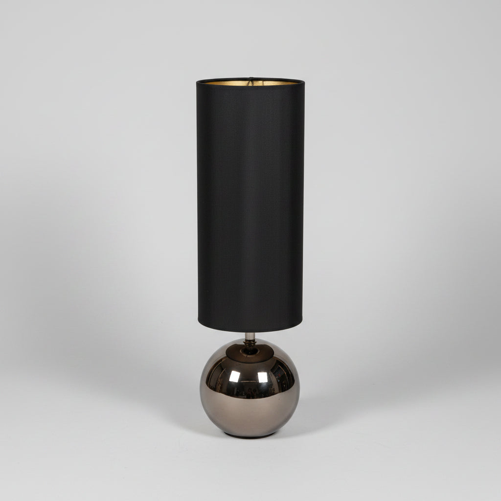 Table lamp with black cylindrical shade and bronze base on a gray surface.